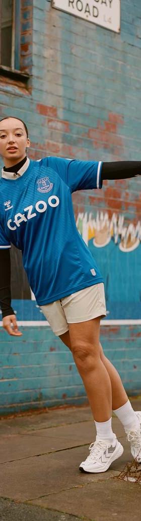 A woman wearing a blue hummel Everton football shirt with white shorts and sneakers on a city street