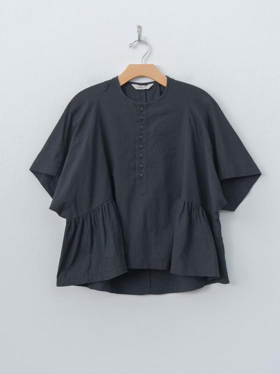 A charcoal Ichi Antiquités linen blouse with flared sleeves and gathered peplum hem, hung against a pale wall