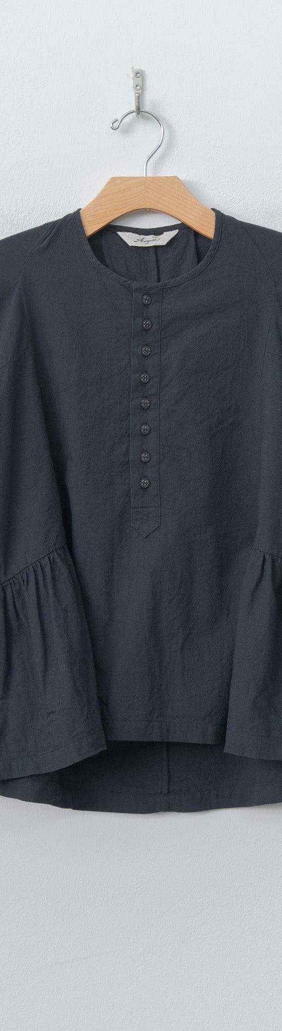 A charcoal Ichi Antiquités linen blouse with flared sleeves and gathered peplum hem, hung against a pale wall