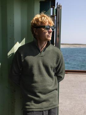 A man wearing a dark green Inis Meáin knitted polo sweater by the sea