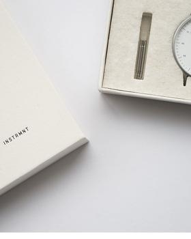 An Instrmnt watch with a white dial and slim steel case presented in its felt-lined box beside a notebook