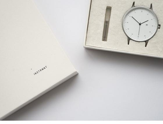 An Instrmnt watch with a white dial and slim steel case presented in its felt-lined box beside a notebook