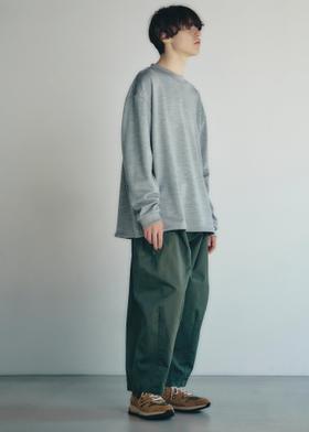 A man wearing a grey oversized long-sleeve knit with wide green trousers