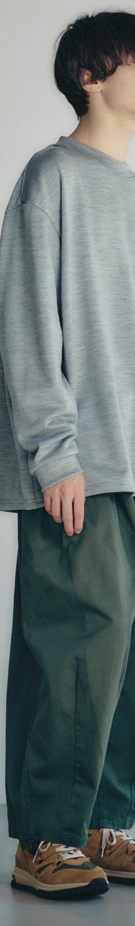 A man wearing a grey oversized long-sleeve knit with wide green trousers