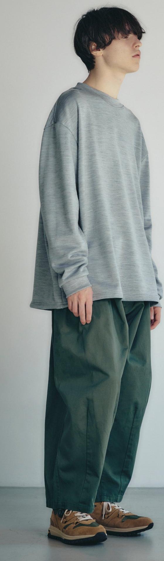 A man wearing a grey oversized long-sleeve knit with wide green trousers