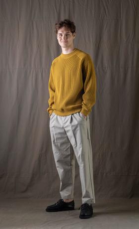 A man wearing a mustard yellow Jackman knit sweater with light grey pleated trousers