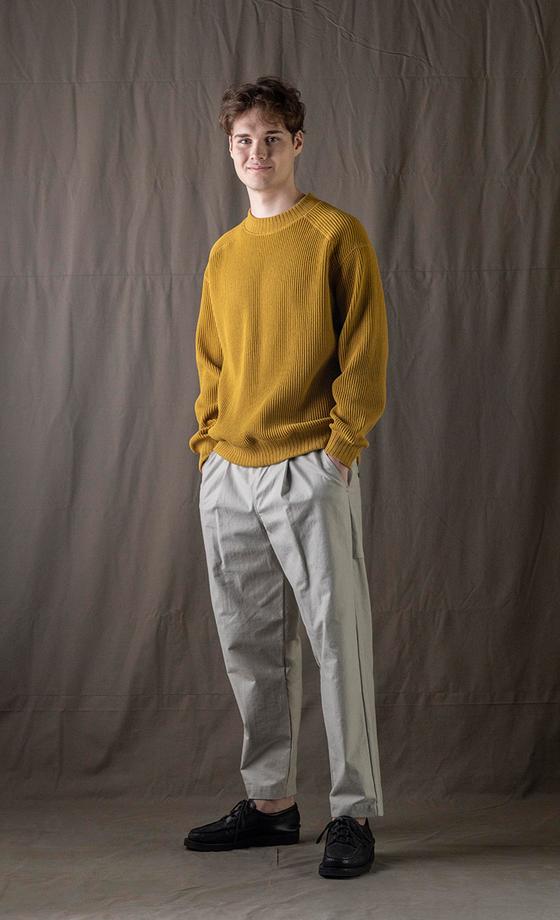 A man wearing a mustard yellow Jackman knit sweater with light grey pleated trousers