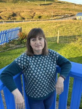 A woman wearing a teal and cream Fair Isle Jamieson's of Shetland sweater outdoors