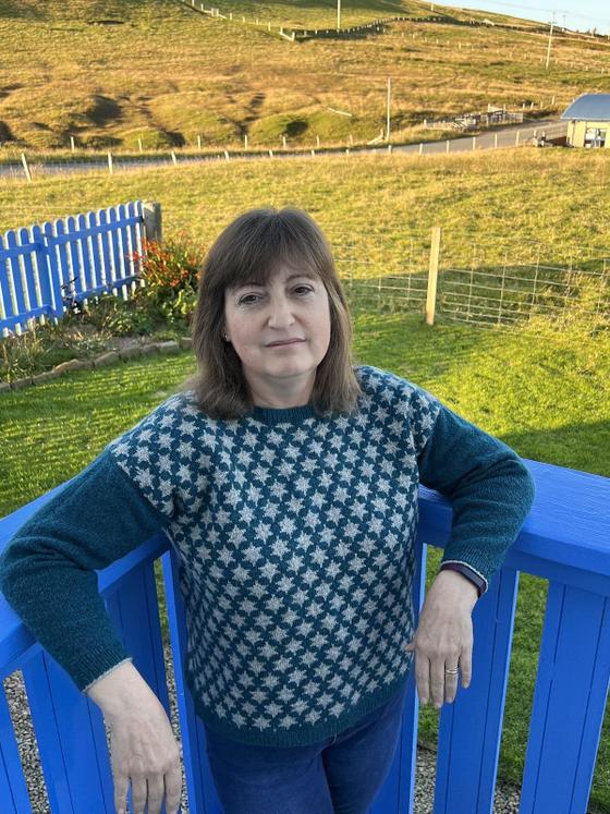 A woman wearing a teal and cream Fair Isle Jamieson's of Shetland sweater outdoors