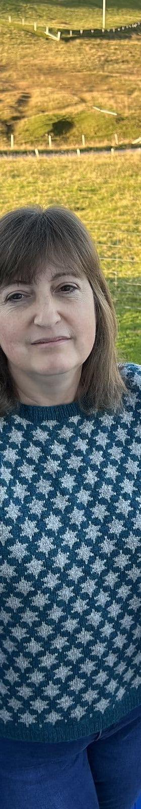 A woman wearing a teal and cream Fair Isle Jamieson's of Shetland sweater outdoors