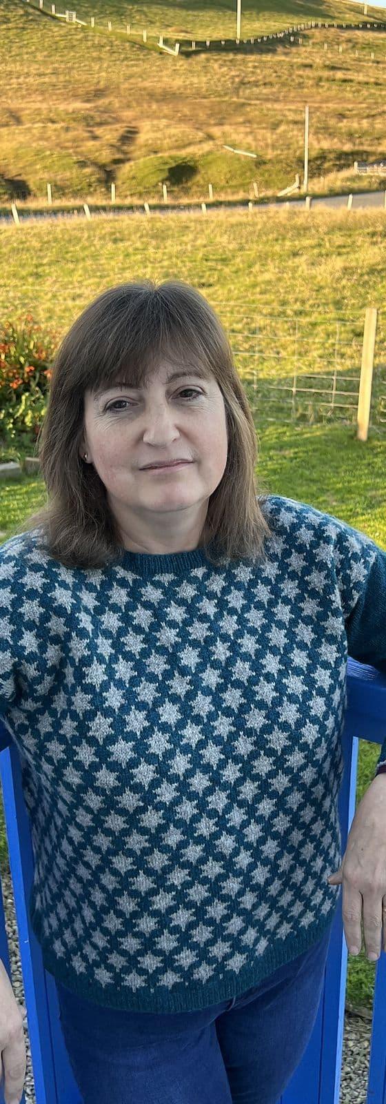 A woman wearing a teal and cream Fair Isle Jamieson's of Shetland sweater outdoors