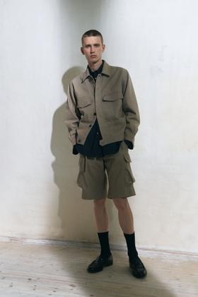 A man wearing a beige Jan Machenhauer utility jacket and matching cargo shorts