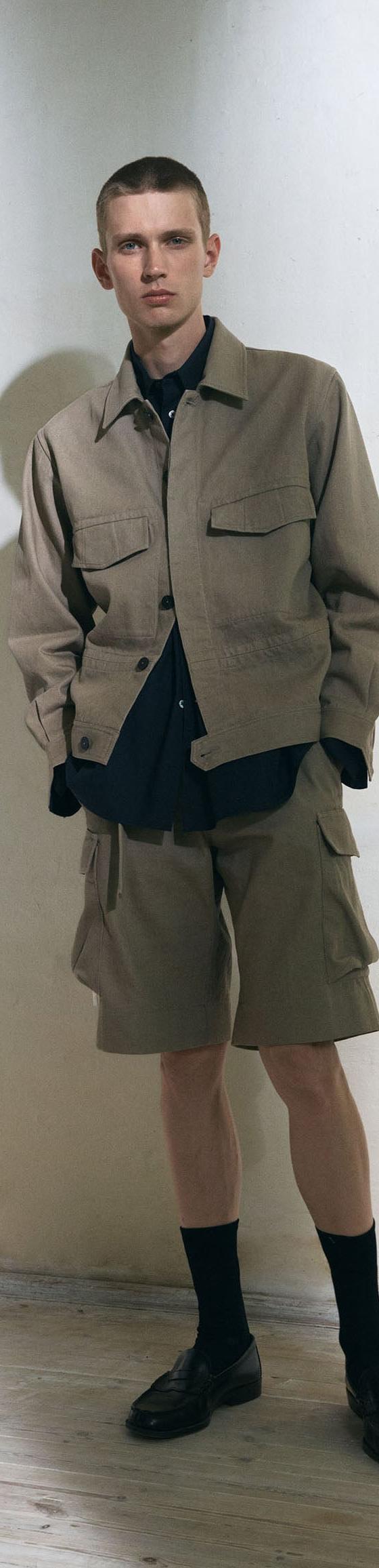 A man wearing a beige Jan Machenhauer utility jacket and matching cargo shorts