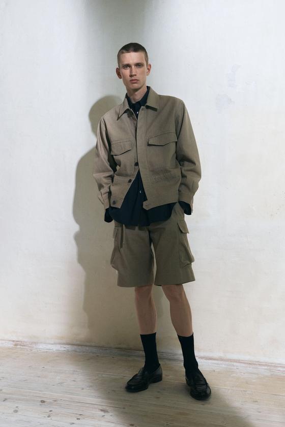 A man wearing a beige Jan Machenhauer utility jacket and matching cargo shorts