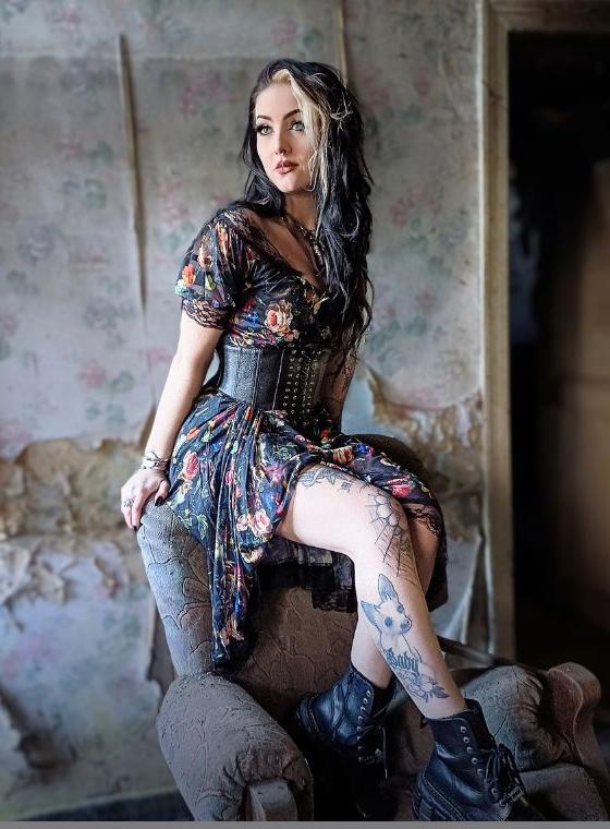 A woman wearing a Jawbreaker Clothing floral print dress with a black underbust corset belt and boots