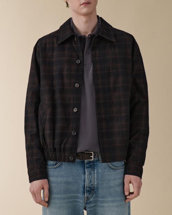 A man wearing a dark checked Jeanerica jacket over a grey polo with blue jeans