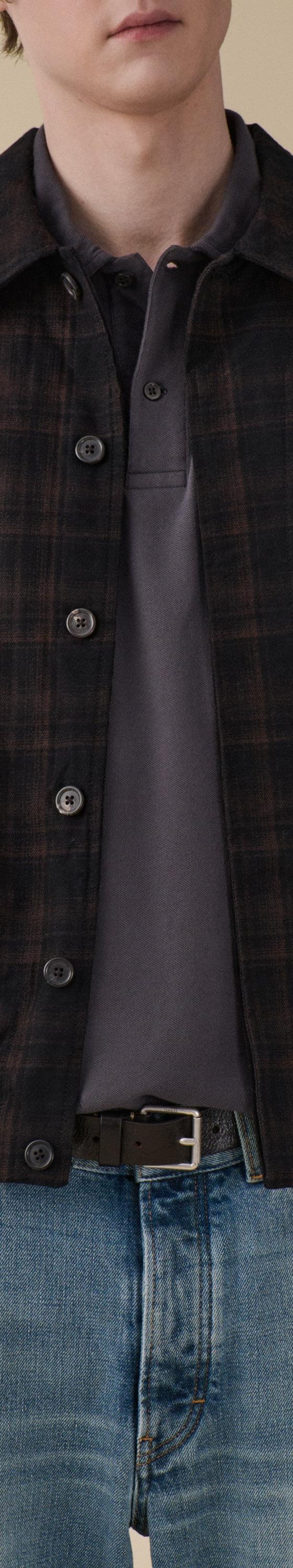 A man wearing a dark checked Jeanerica jacket over a grey polo with blue jeans