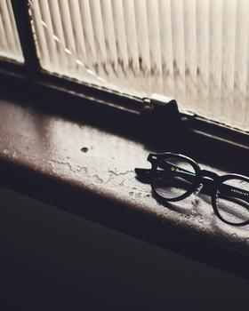 A pair of black acetate Kaneko Optical round eyeglasses resting on a sunlit windowsill