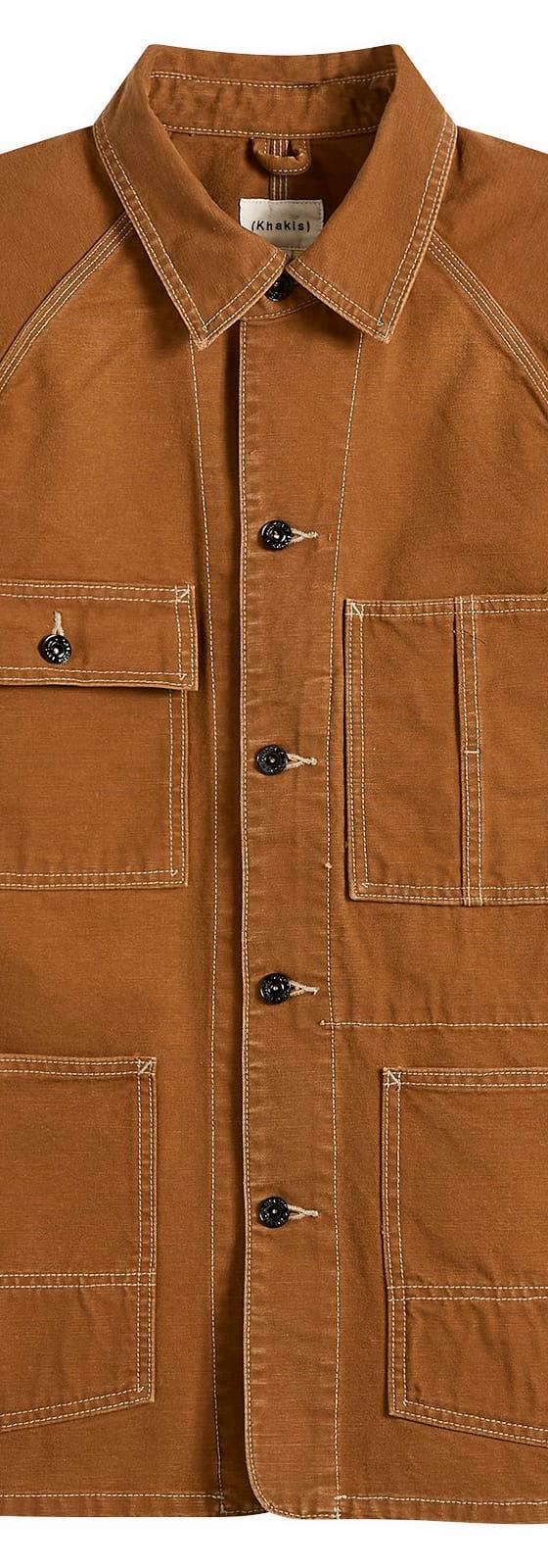 A brown Khakis chore jacket with contrast stitching on a plain background