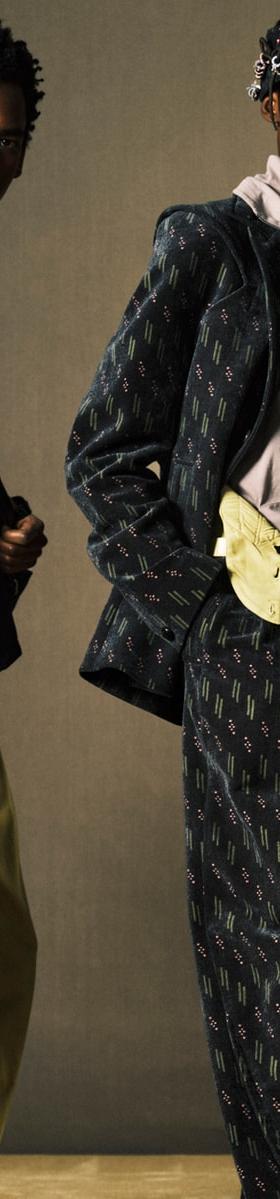 Two models wearing Kijun tailoring, a black utility vest with yellow trousers and a printed suit with a headscarf