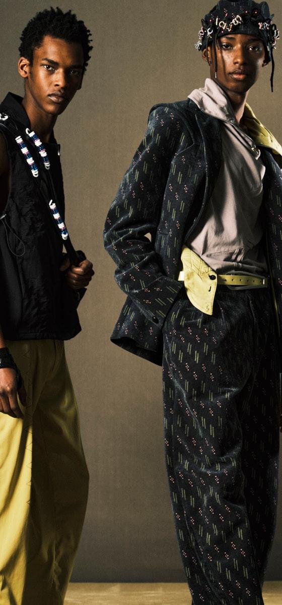 Two models wearing Kijun tailoring, a black utility vest with yellow trousers and a printed suit with a headscarf