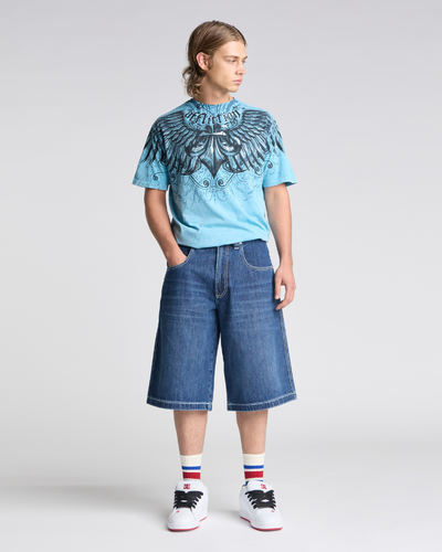 A man wearing a blue graphic tee and wide-leg Kikwear denim shorts