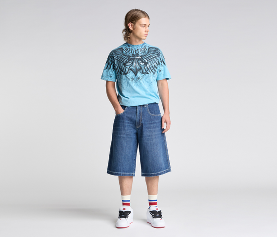 A man wearing a blue graphic tee and wide-leg Kikwear denim shorts