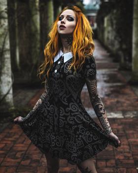 A woman wearing a black occult-print Killstar collared dress in a stone colonnade