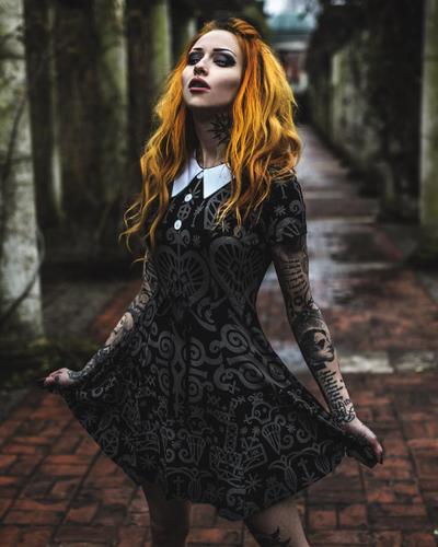 A woman wearing a black occult-print Killstar collared dress in a stone colonnade