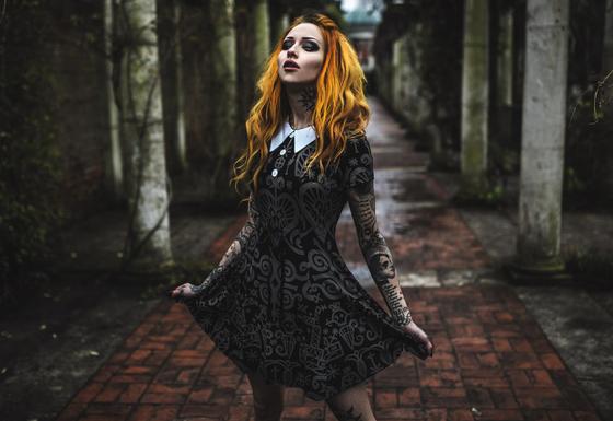 A woman wearing a black occult-print Killstar collared dress in a stone colonnade