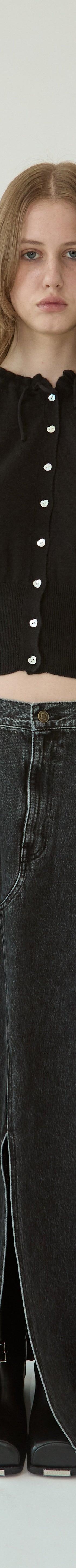 A woman wearing a black KIMHĒKIM cropped cardigan with pearl buttons and a long washed black denim skirt
