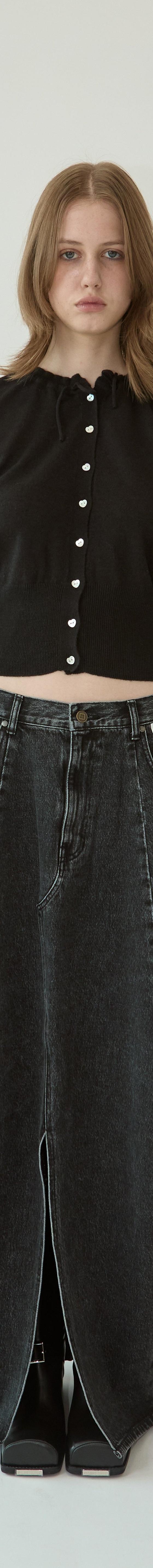 A woman wearing a black KIMHĒKIM cropped cardigan with pearl buttons and a long washed black denim skirt