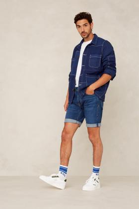 A man wearing a blue Kings Of Indigo denim chore jacket and denim shorts