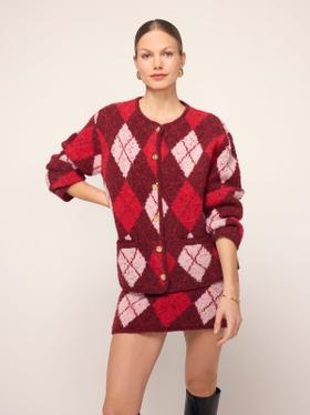 A woman wearing a red and pink argyle KITRI knit cardigan and matching mini skirt with black knee boots