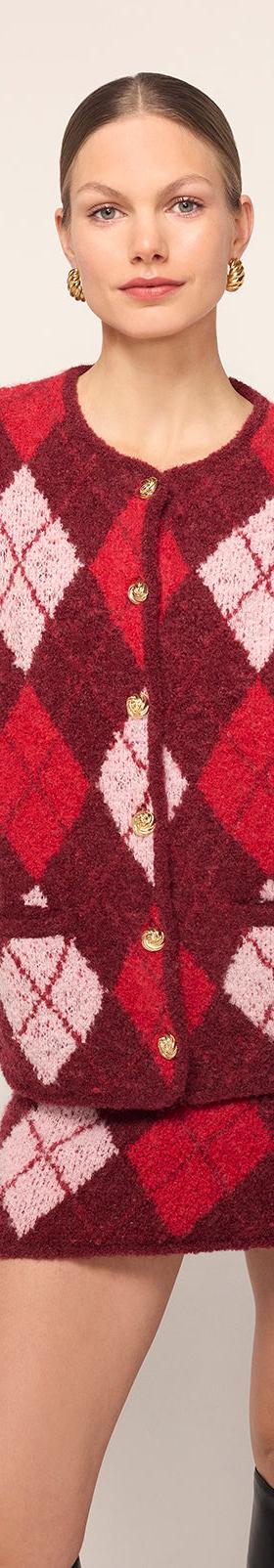 A woman wearing a red and pink argyle KITRI knit cardigan and matching mini skirt with black knee boots