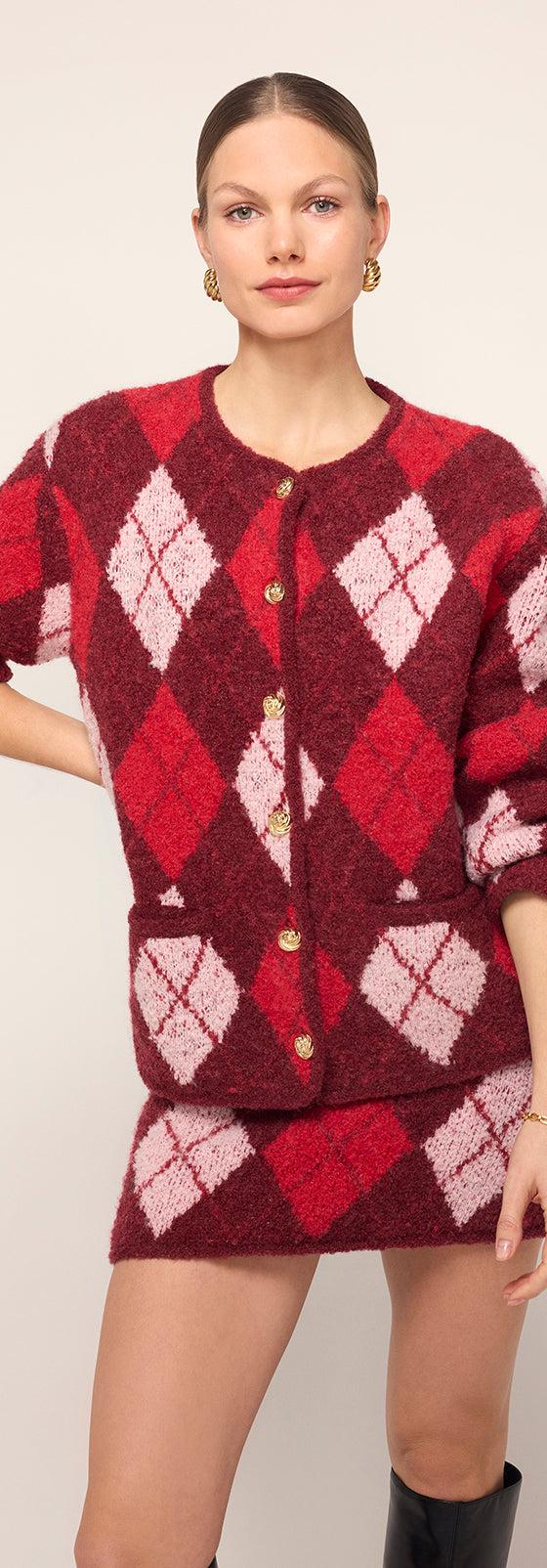A woman wearing a red and pink argyle KITRI knit cardigan and matching mini skirt with black knee boots