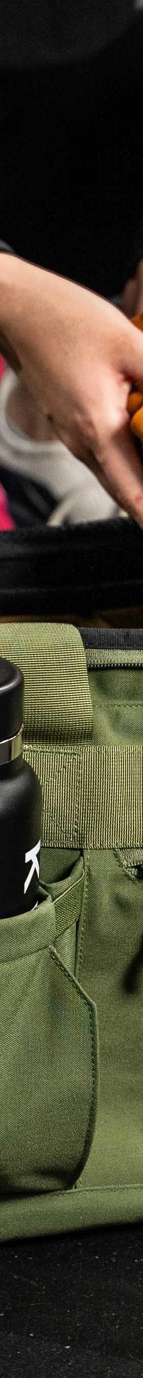 A woman crouching beside an olive green KNKG gym duffel bag on a gym floor