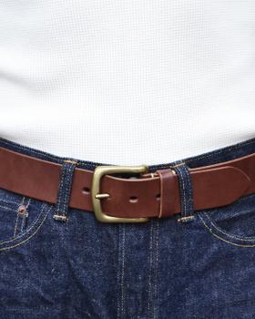 A person wearing a brown leather Kobashi Studio belt with a solid-brass buckle over indigo denim