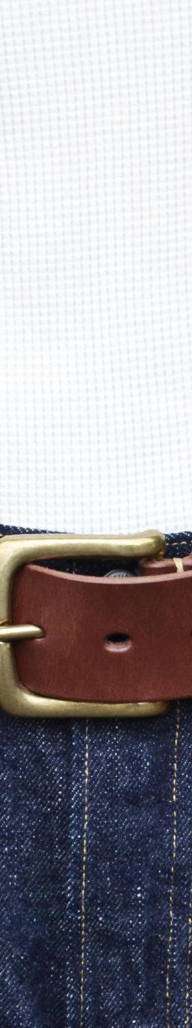 A person wearing a brown leather Kobashi Studio belt with a solid-brass buckle over indigo denim