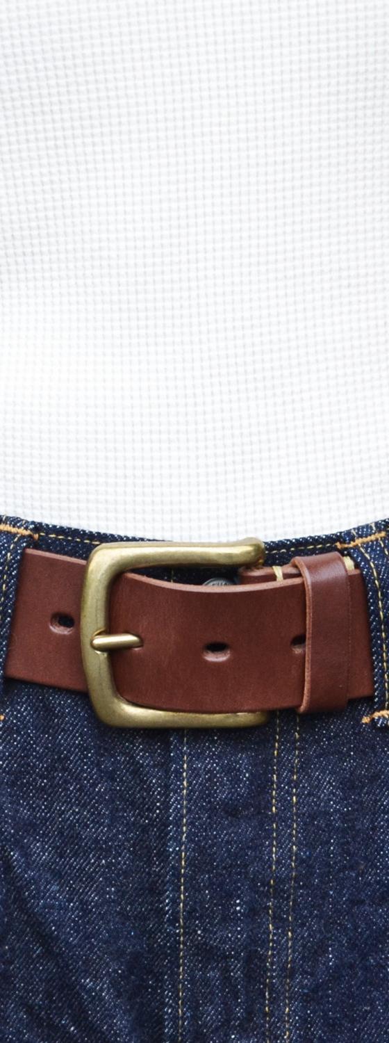 A person wearing a brown leather Kobashi Studio belt with a solid-brass buckle over indigo denim