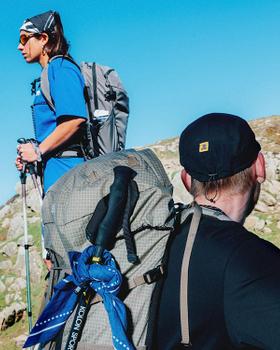 Two men hiking with Kolon Sport backpacks and outdoor gear on a grassy hillside