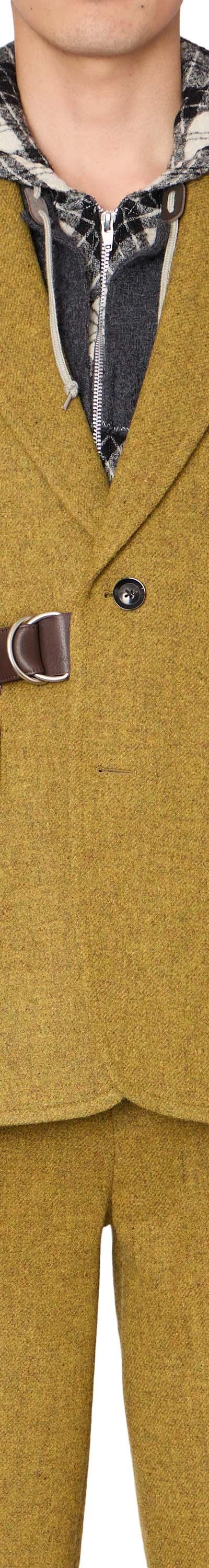 A man wearing a mustard yellow kolor tweed blazer with a leather belt strap and layered check hooded shirt