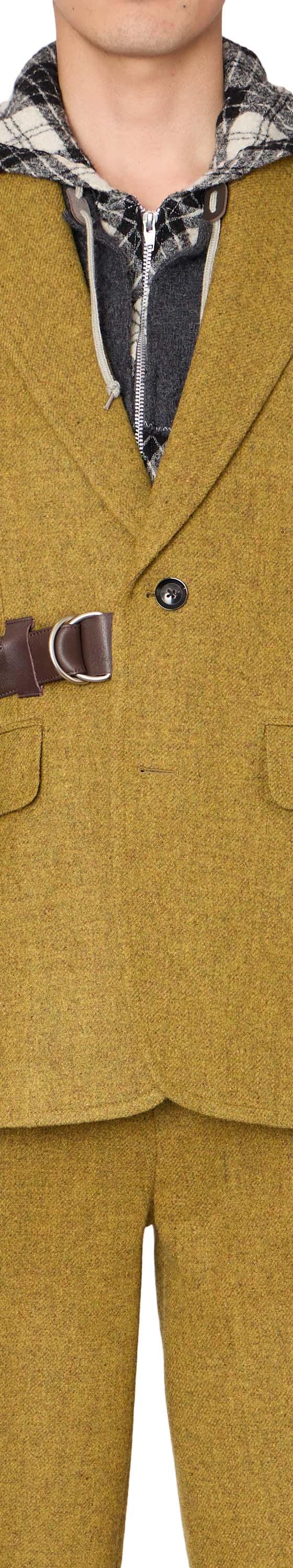 A man wearing a mustard yellow kolor tweed blazer with a leather belt strap and layered check hooded shirt