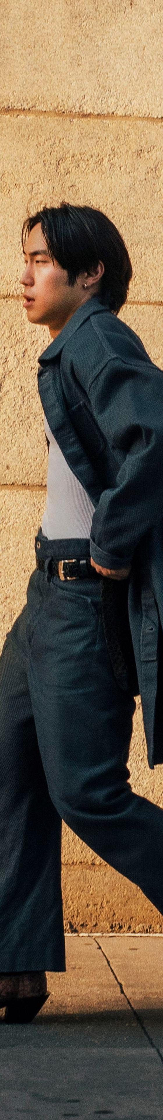 A man wearing a Kozaburo indigo denim coat with wide-leg jeans and curved-heel snakeskin boots