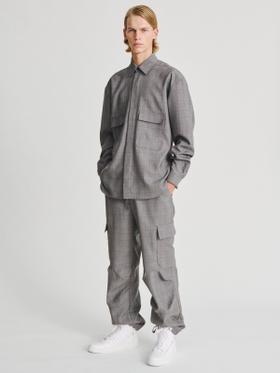 A man wearing a grey check Kris Van Assche overshirt and matching cargo trousers