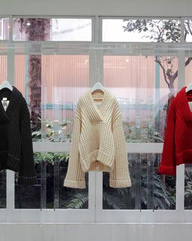 Shop window display: three archive coats (black, cream, red) on hangers against the glass, no people