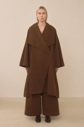 A woman wearing a brown oversized Lauren Manoogian wrap coat and wide-leg trousers