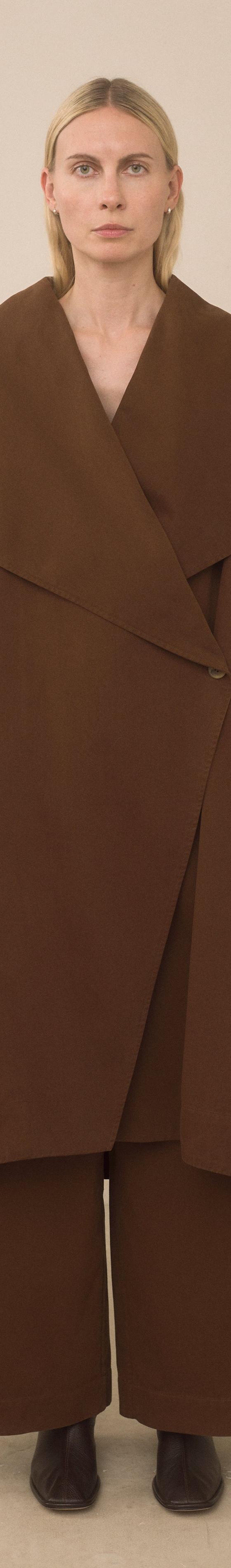 A woman wearing a brown oversized Lauren Manoogian wrap coat and wide-leg trousers