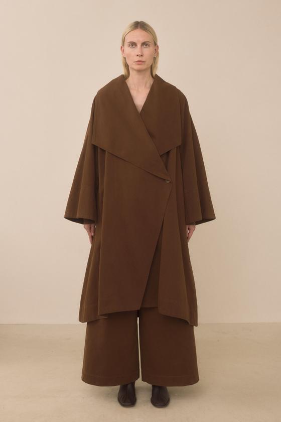 A woman wearing a brown oversized Lauren Manoogian wrap coat and wide-leg trousers