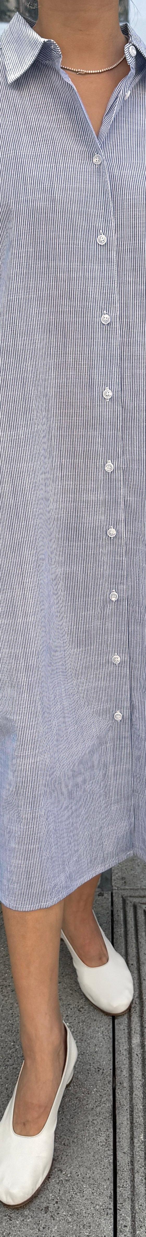 A woman wearing a pale blue striped Le Bon Shoppe shirt dress with white flats